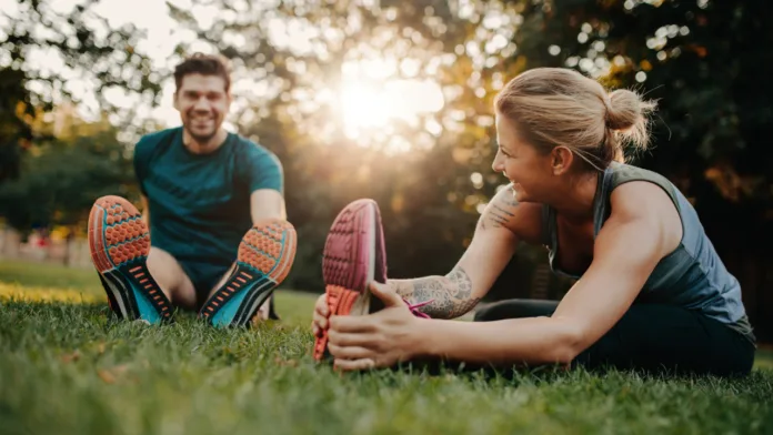 Man and woman stretching together in a park during sunset, promoting physical and mental well-being.